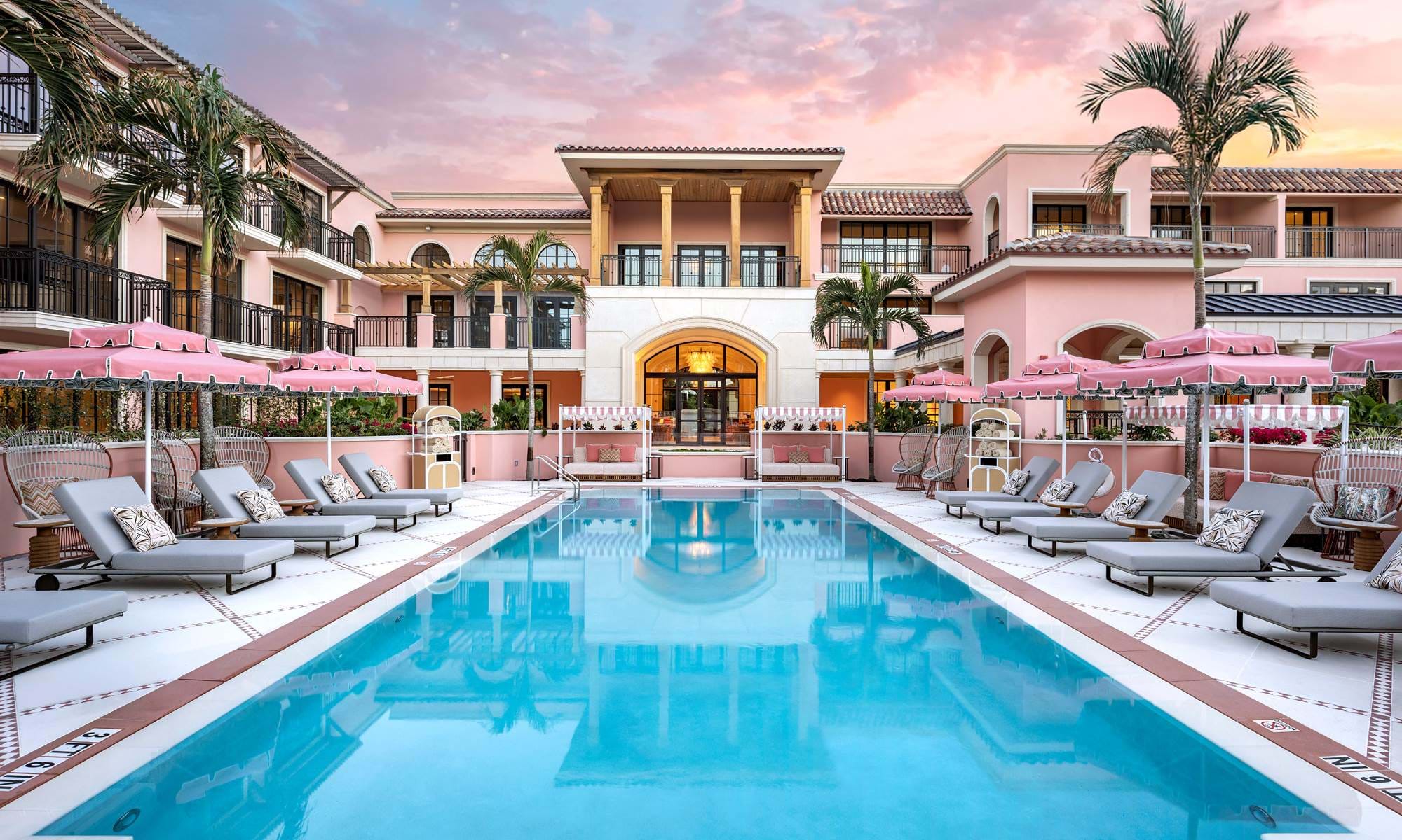 Pink umbrellas and lounge chairs surrounding the pool at Palm House in Palm Beach